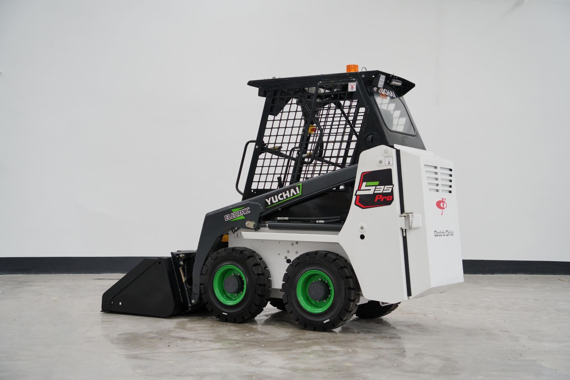 White and black YUCHAI S25 skid steer loader with green wheels and a black bucket in a bright room.