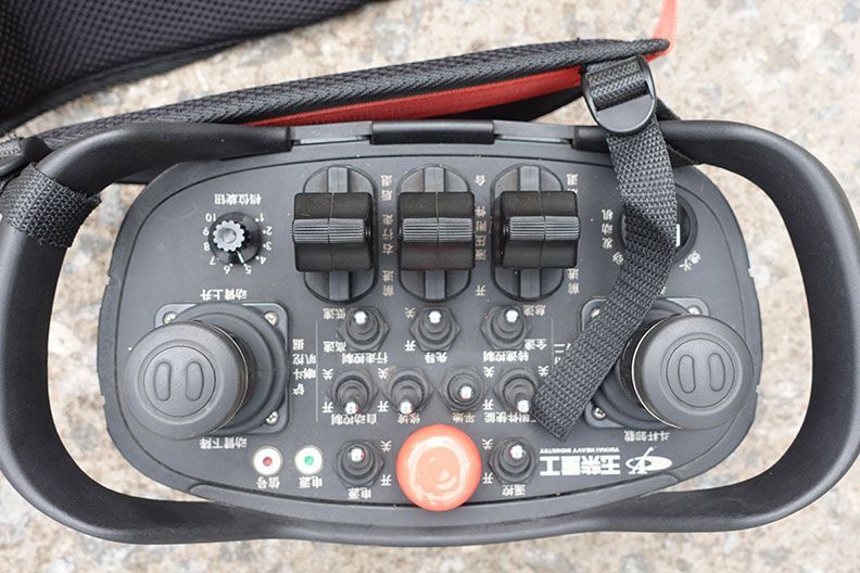 Télécommande noire avec plusieurs interrupteurs et joysticks. Bouton d'arrêt d'urgence rouge. Dragonne noire.