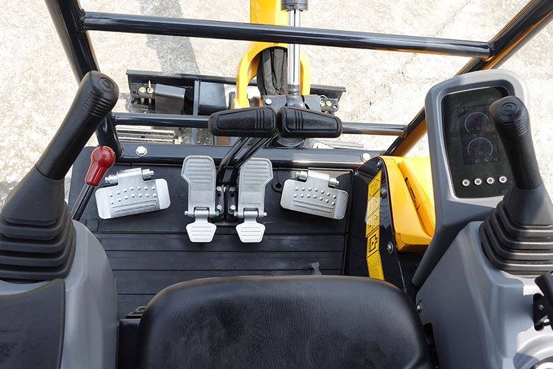 Vue intérieure de la cabine d'une excavatrice, montrant les joysticks, les pédales et un écran d'affichage.