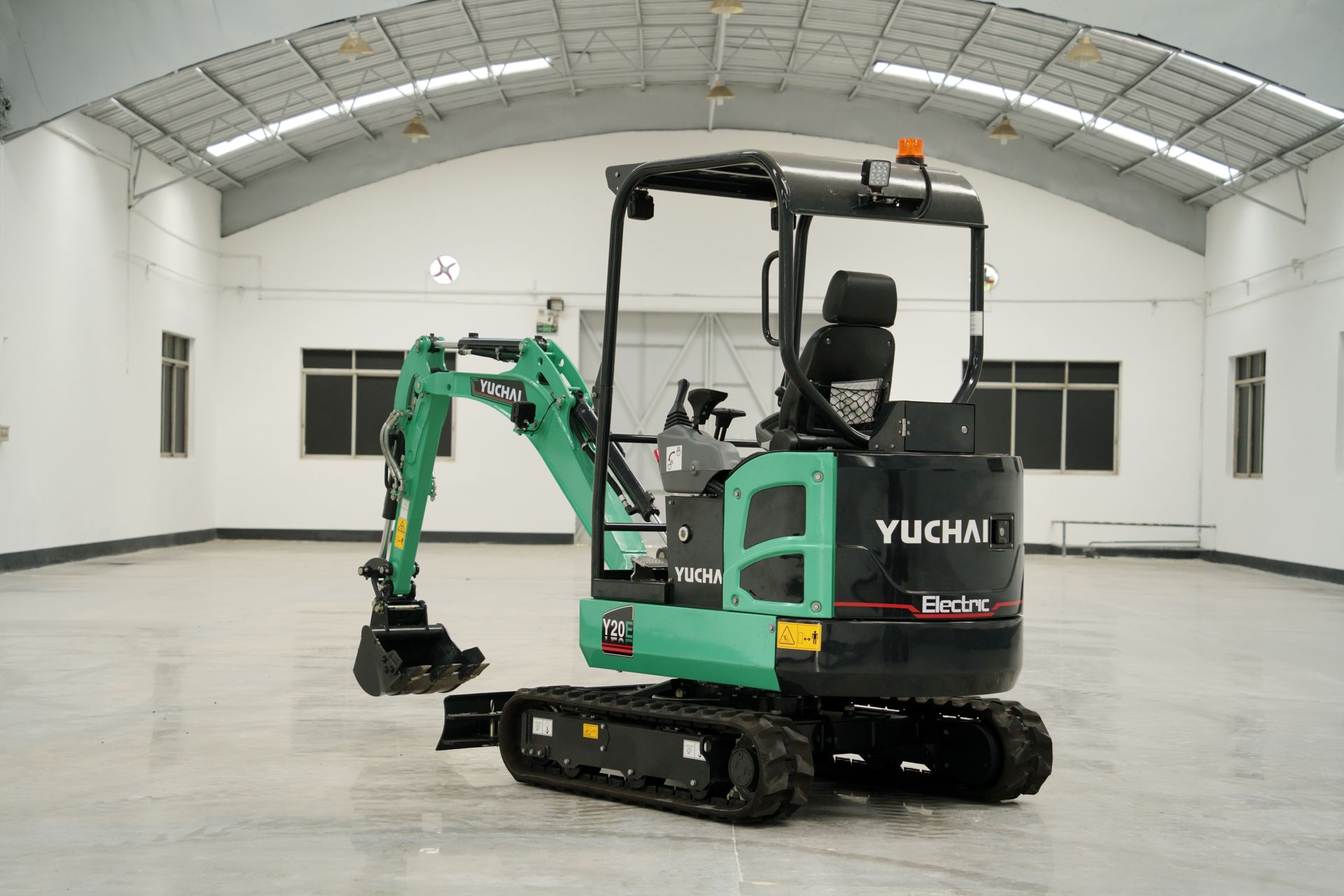 Green and black YUCHAI YC20E mini excavator inside a white warehouse.