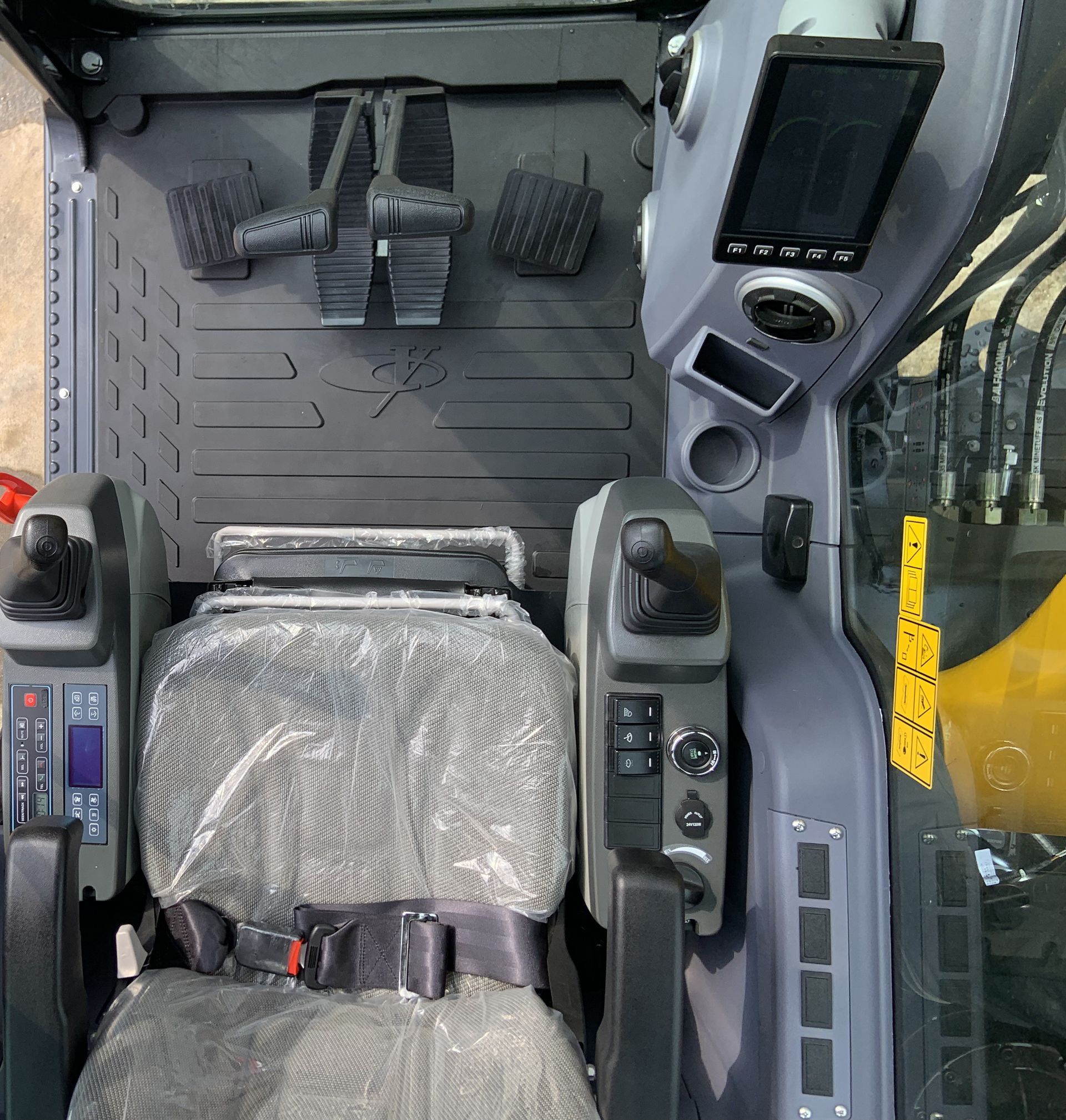 Intérieur de la cabine d'une machine lourde avec siège, commandes et écran. Gris et noir avec des touches de jaune.