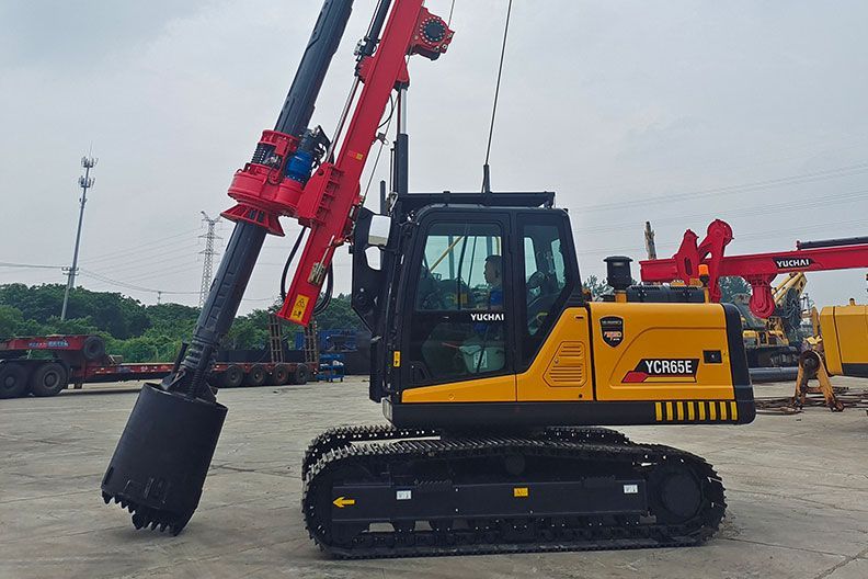 Yellow and black YUCHAI YCR65E drilling rig on tracks, with a red drill head, outdoors.