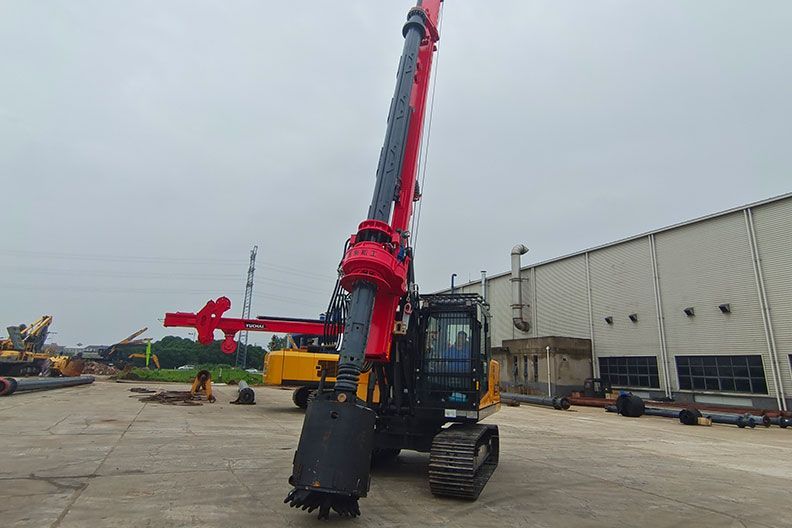 A large YUCHAI YCR65E drilling machine with an extended arm, near a building on a concrete surface.
