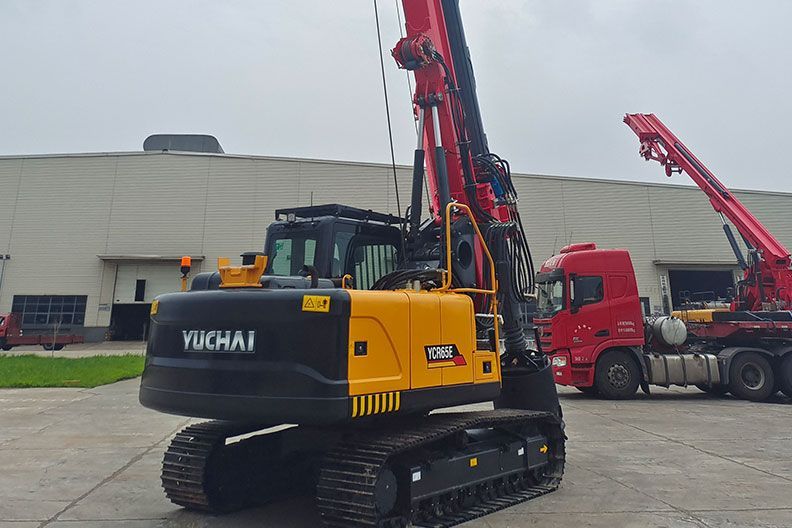 Yellow and black Yuchai YCR65E drilling machine on tracks, with red components, next to a building and a red truck.