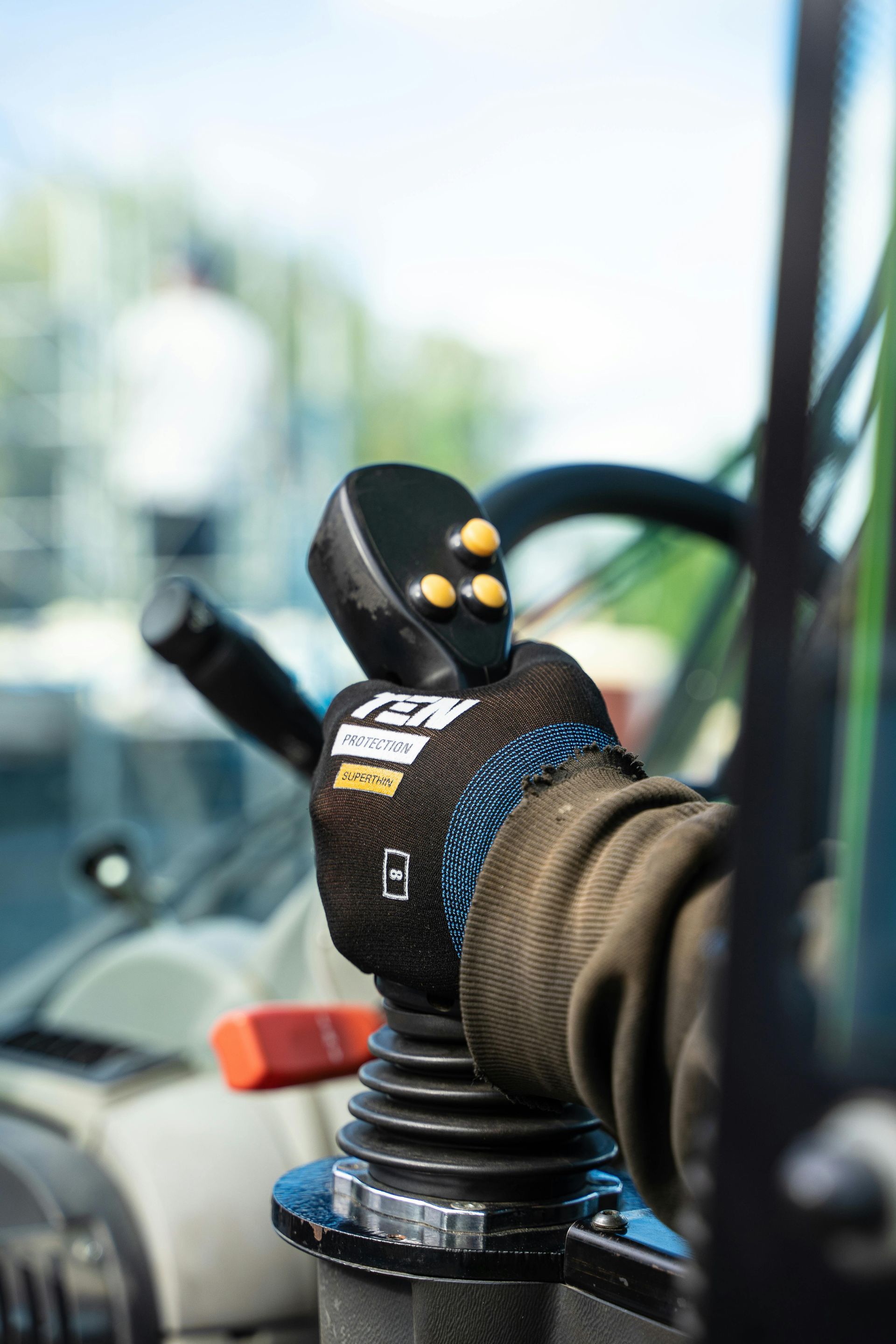Gloved hand operating a joystick control inside a vehicle cab, with buttons and levers visible.
