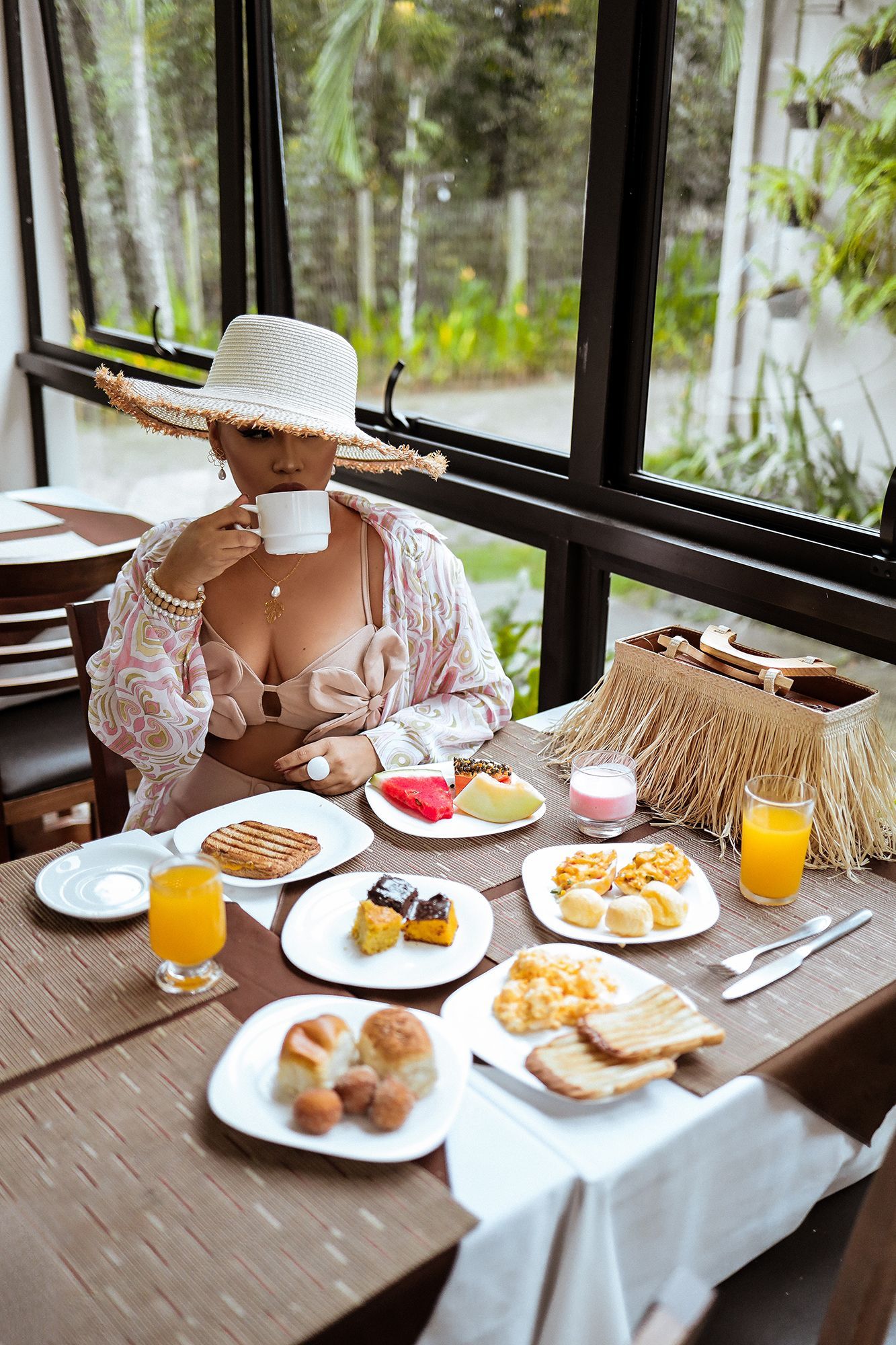 Uma mulher está sentada à mesa com pratos de comida e bebidas.
