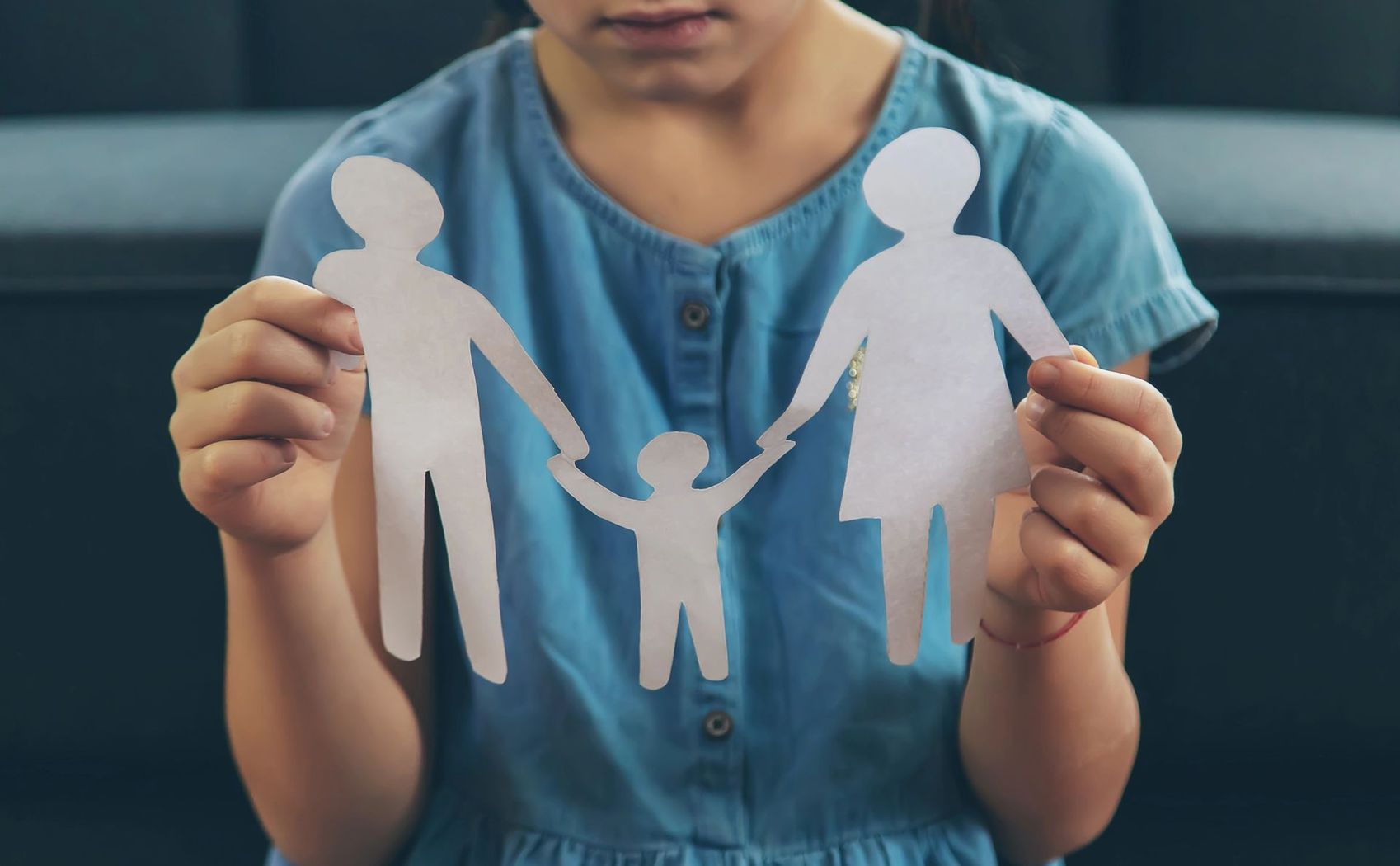 Bambino che tiene in mano sagome di carta bianca raffiguranti membri della famiglia, su uno sfondo blu simile a una maglietta.