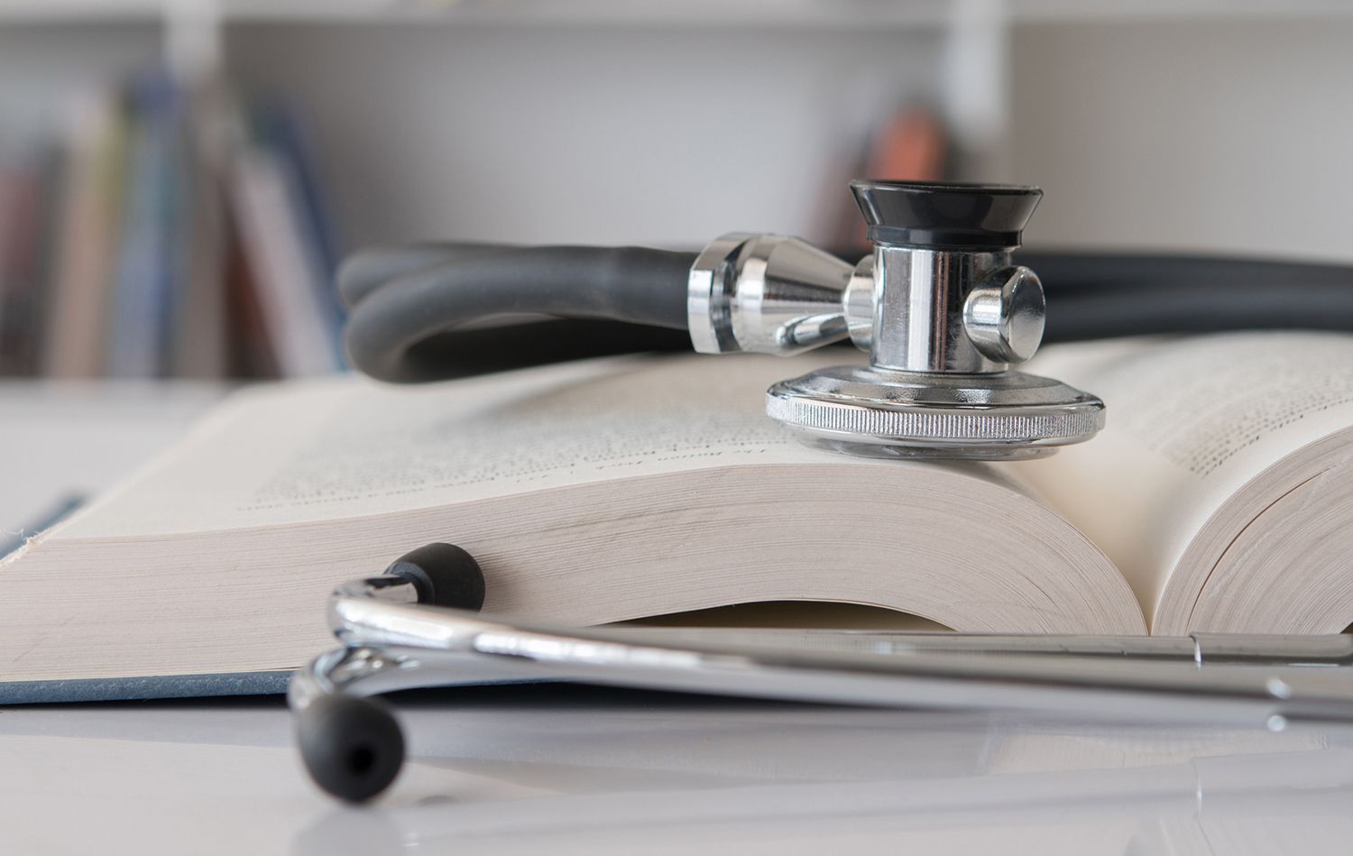 Stethoscope resting on an open book, possibly a medical textbook, on a desk. Stethoscope resting on an open book, possibly a medical textbook, on a desk.