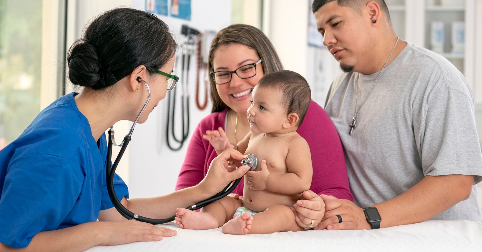 Doctor shaking hands with a woman in a waiting room, blue chairs, patterned wall. Doctor examines baby with stethoscope, parents watching at clinic.