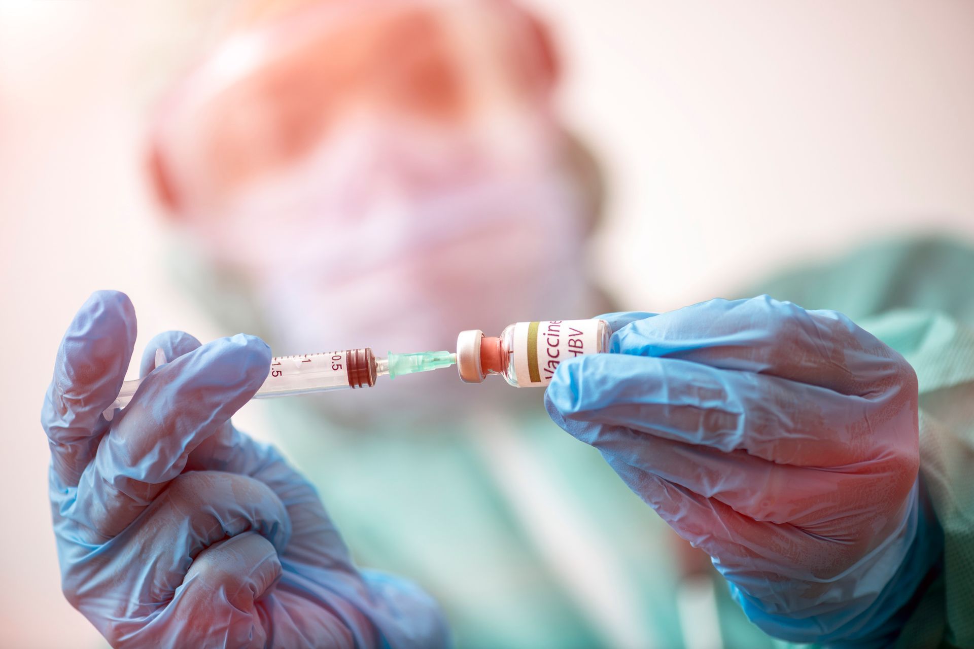 Medical professional filling syringe from vial, wearing gloves and scrubs.
