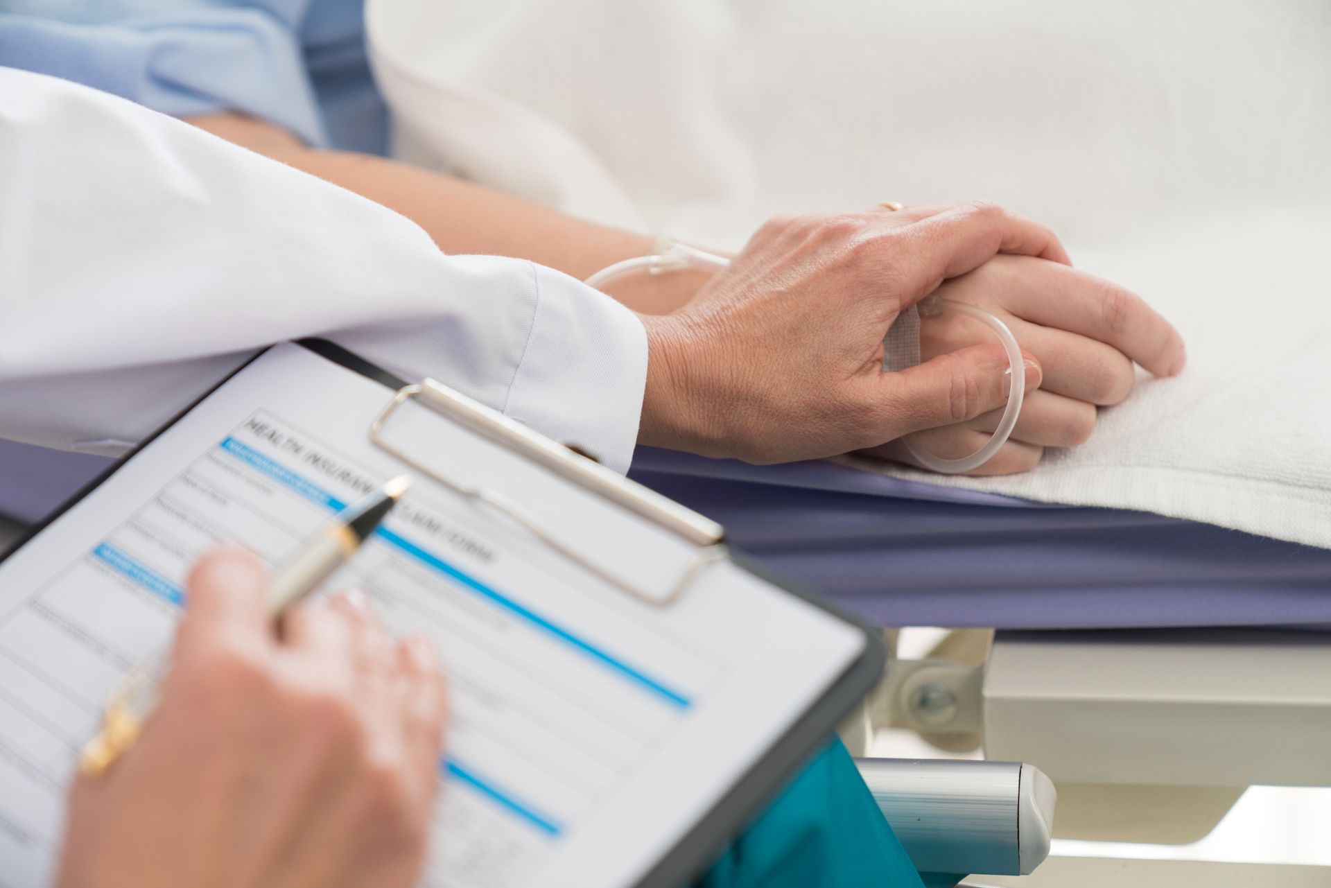 Doctor holding a patient's hand and reviewing medical charts in a hospital setting.