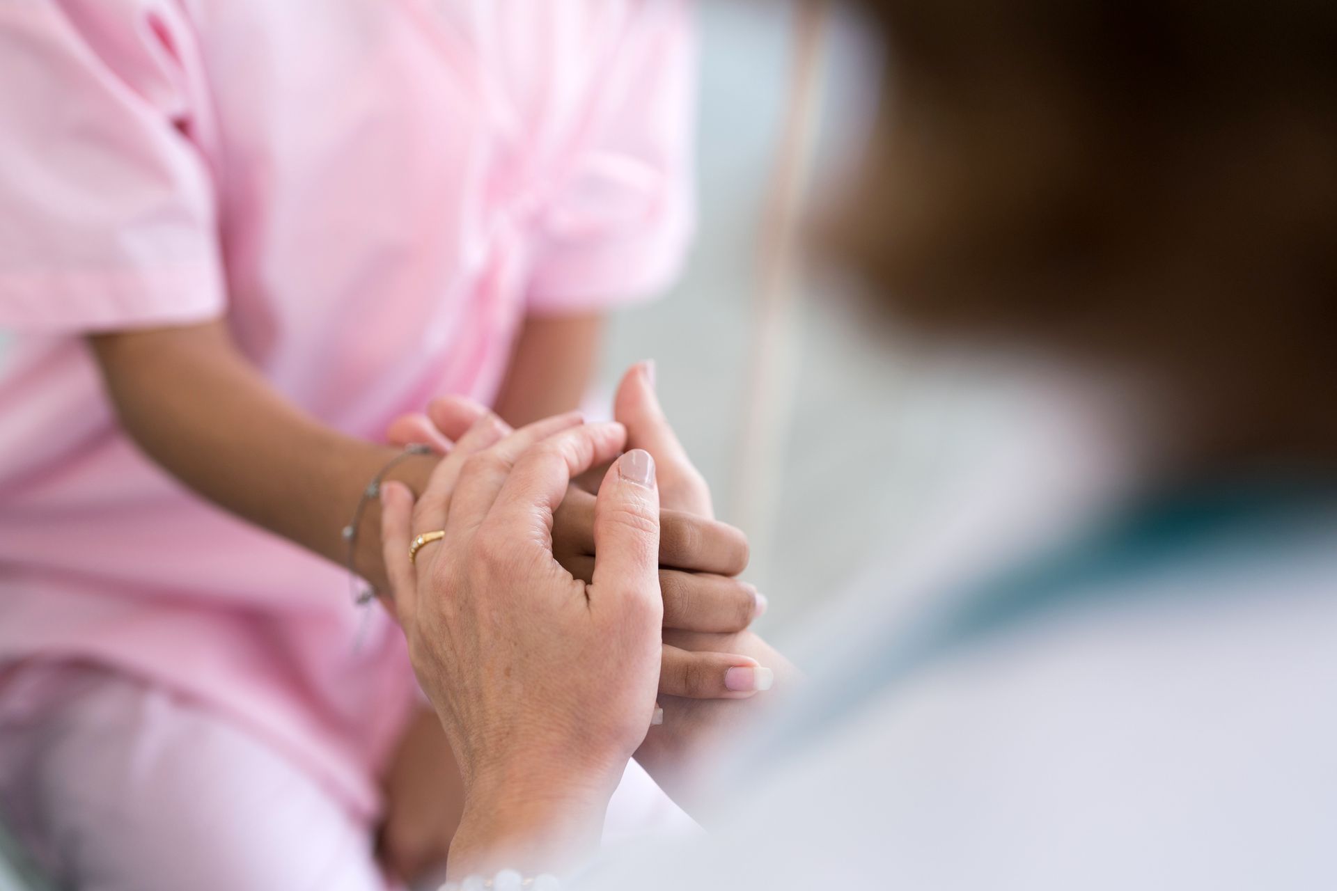 Doctor holds a patient's hand for comfort, both are indoors.