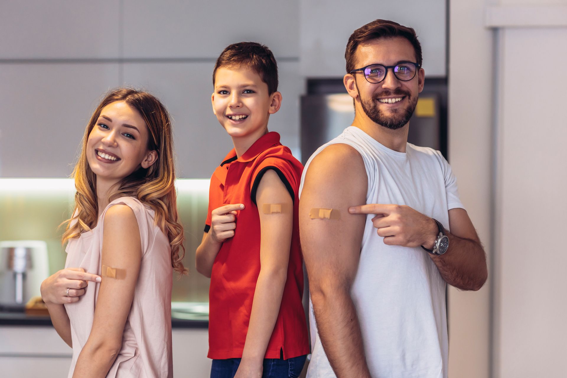 Family points at their arms with adhesive bandages; they are smiling. Inside a home. Family points at their arms with adhesive bandages; they are smiling. Inside a home.