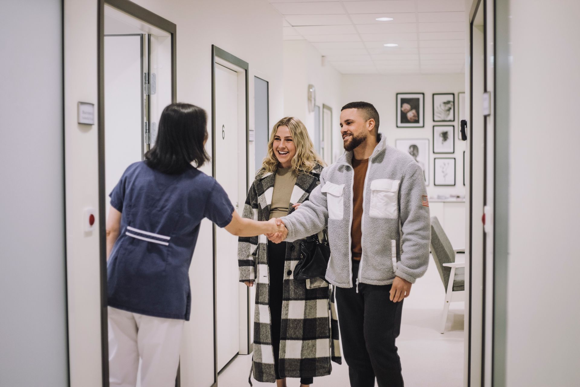 A healthcare worker shakes hands with a couple in a clinic hallway. A healthcare worker shakes hands with a couple in a clinic hallway.