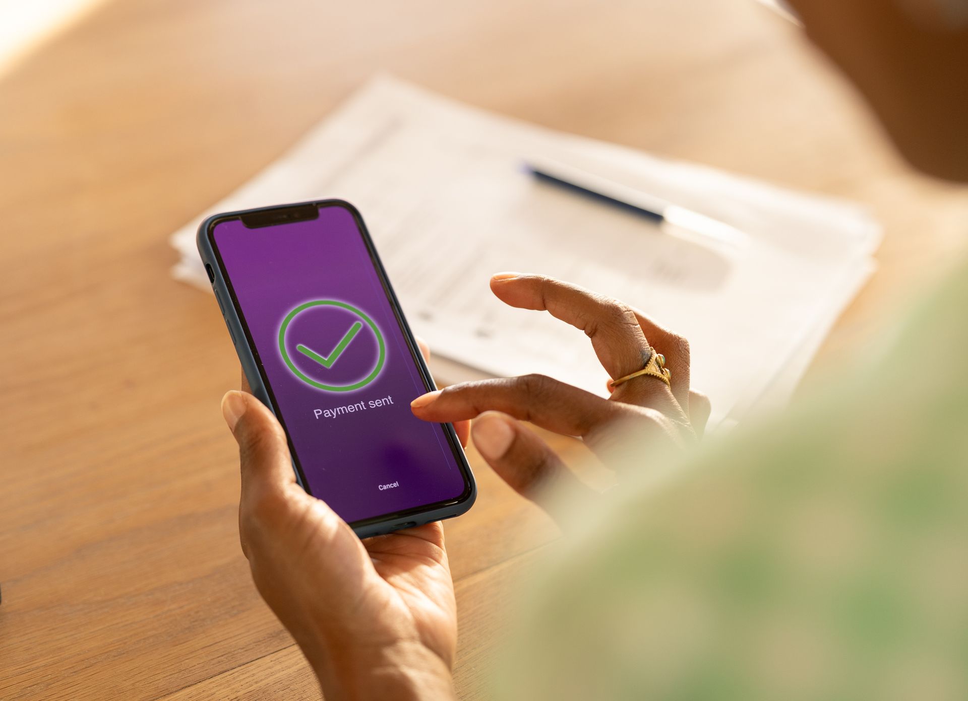 Person holding a smartphone displaying a checkmark on a purple screen, next to papers and a pen.