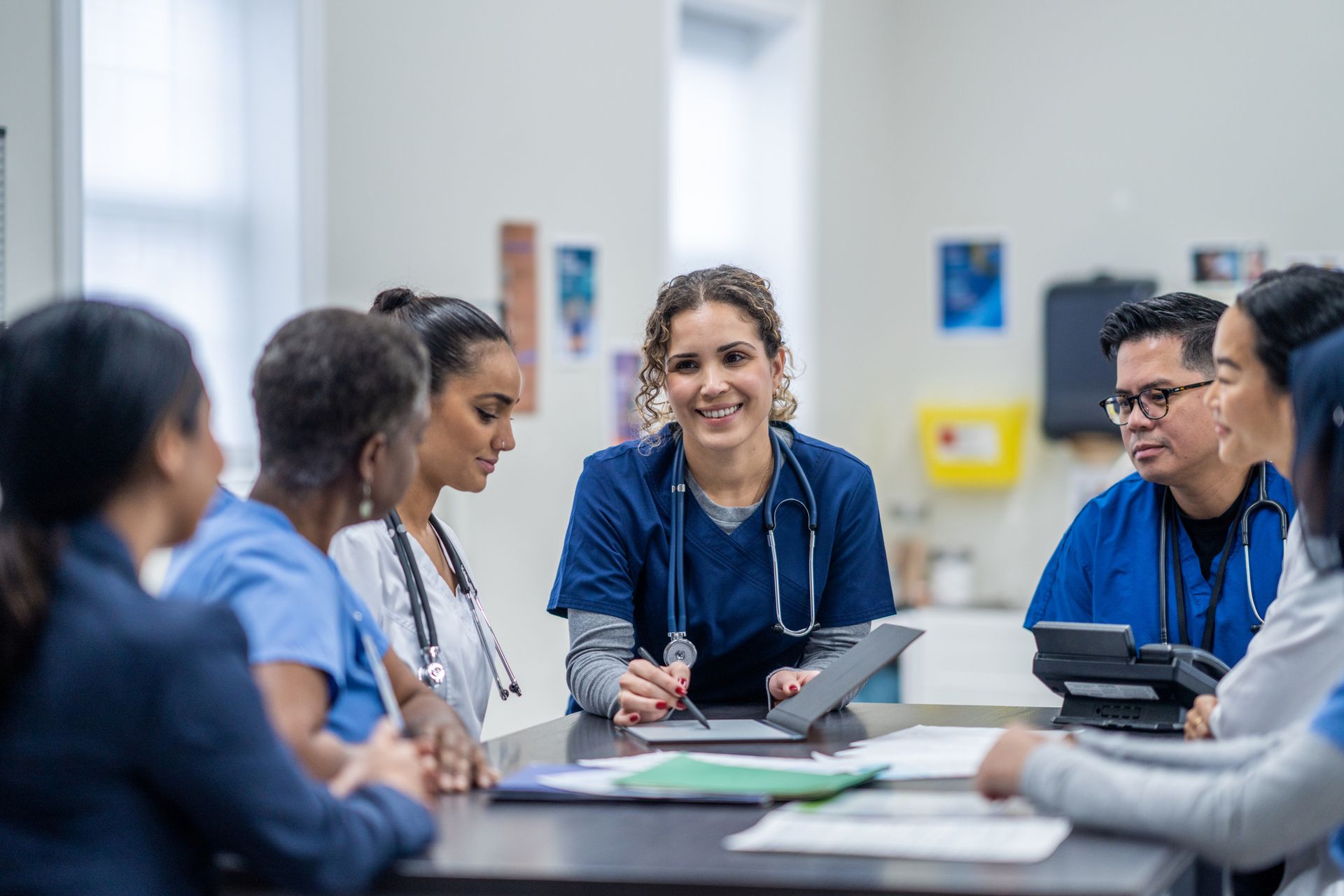 Medical team in blue scrubs at a table, smiling and looking at a tablet.