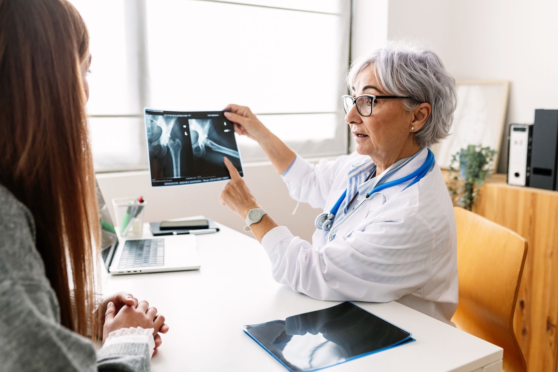 Doctor points to X-ray, explaining to patient at a desk in a medical office. Doctor points to X-ray, explaining to patient at a desk in a medical office.