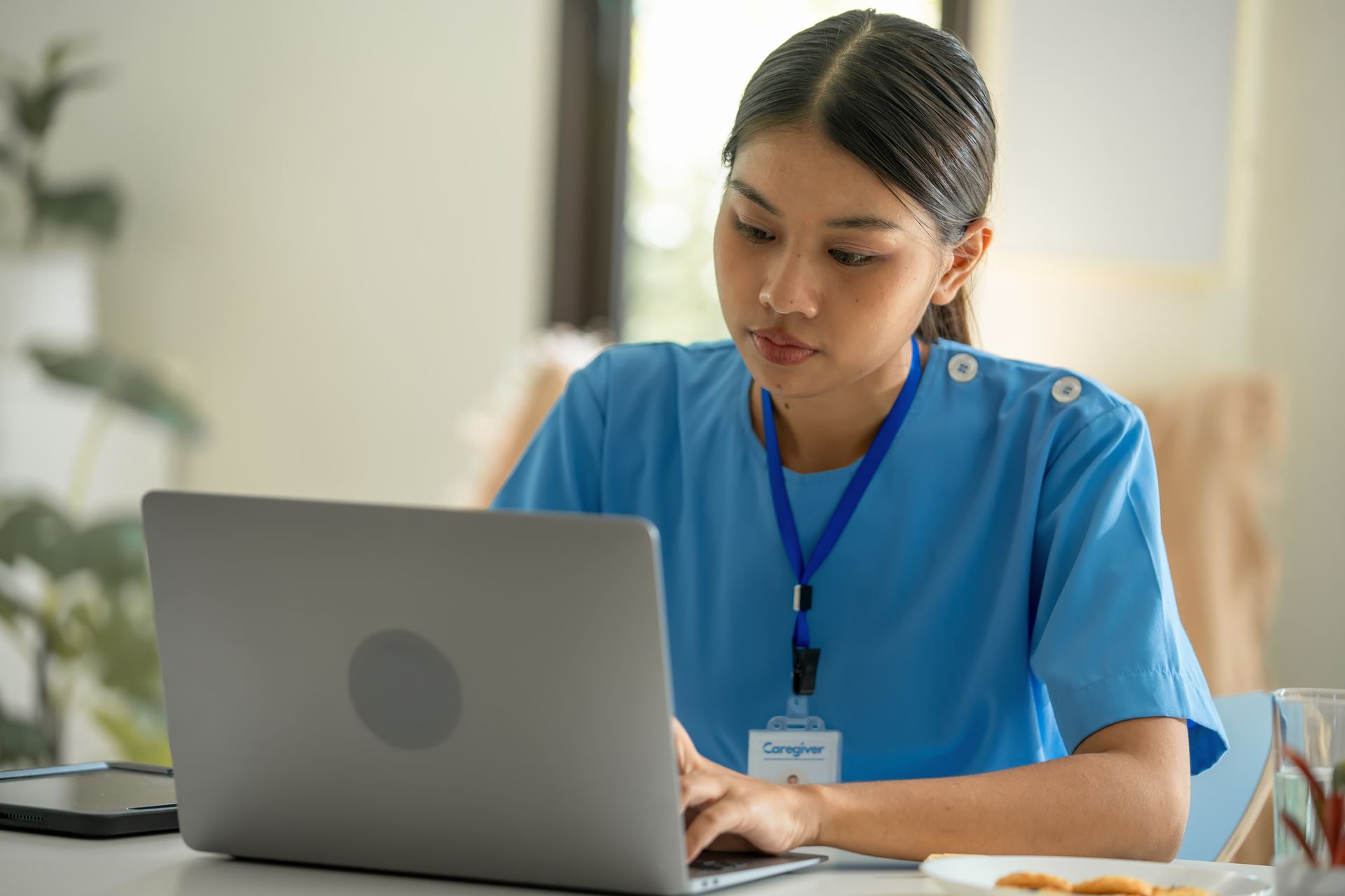 Woman in blue uniform working on a laptop indoors.