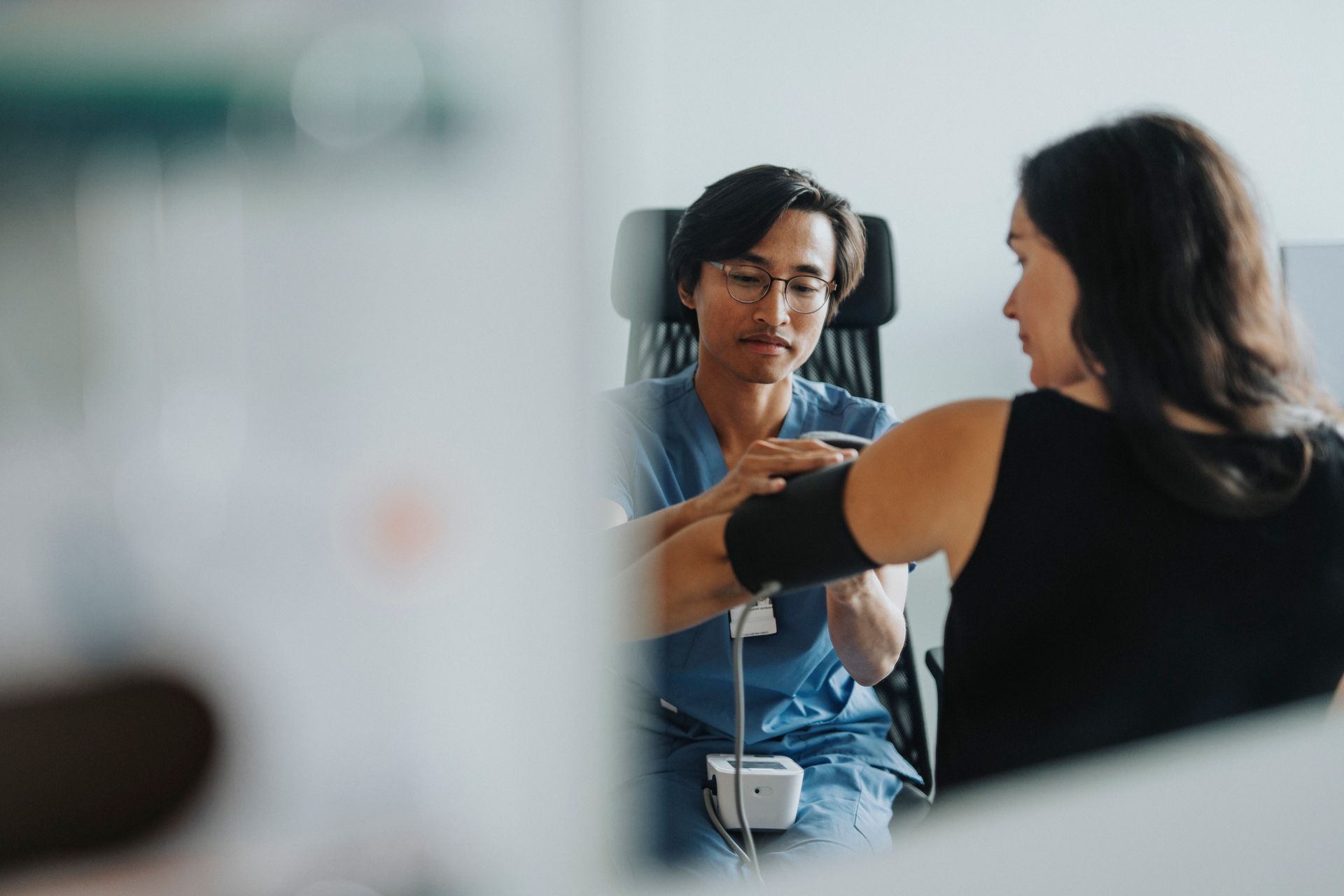 Doctor taking patient's blood pressure in an office. Doctor is wearing glasses and a blue uniform. Doctor taking patient's blood pressure in an office. Doctor is wearing glasses and a blue uniform.
