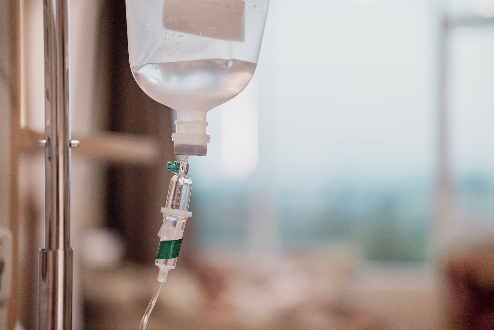 IV drip bag with clear liquid hanging in a hospital room.