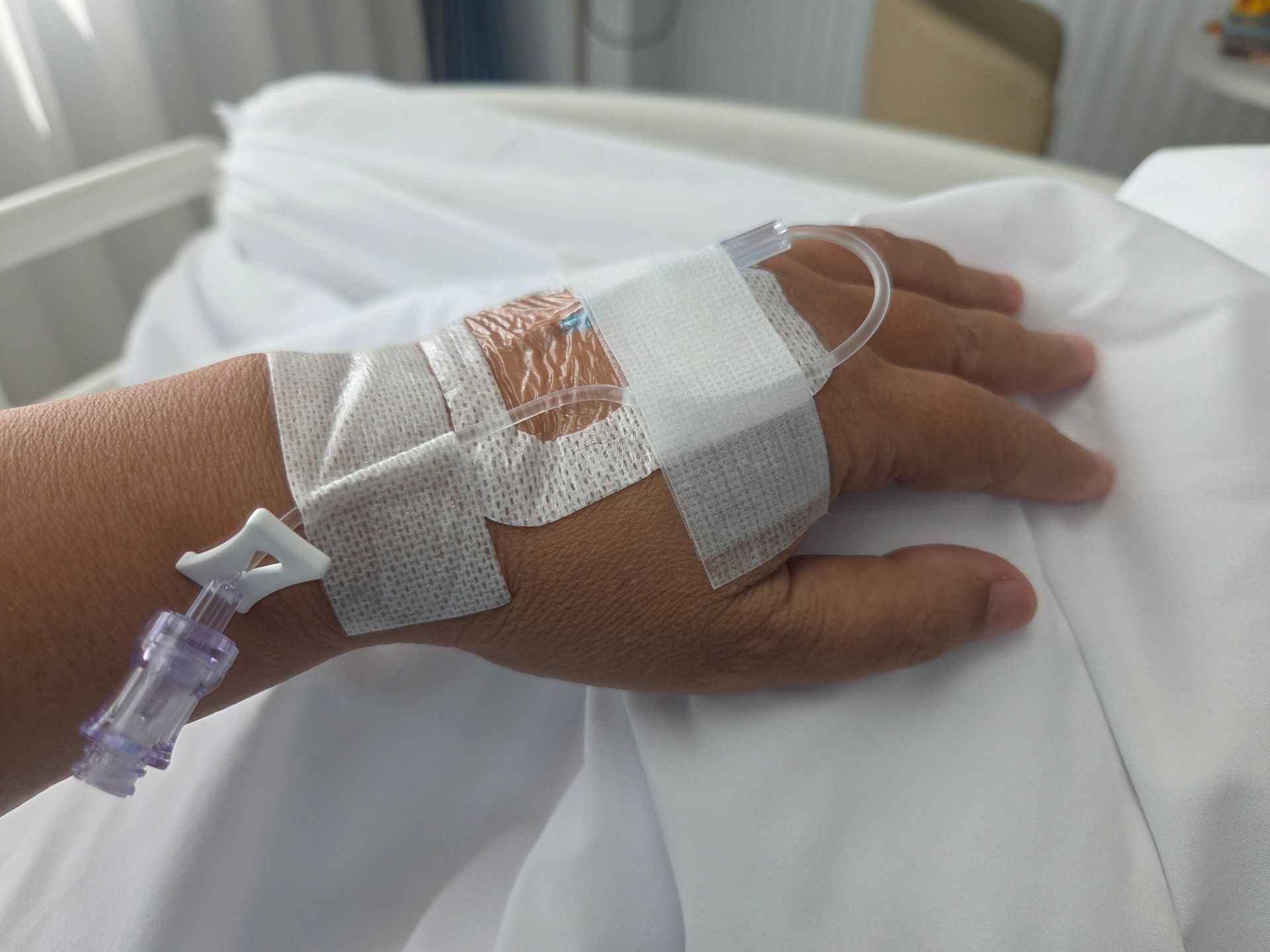 Hand with IV in hospital bed, taped to the wrist.