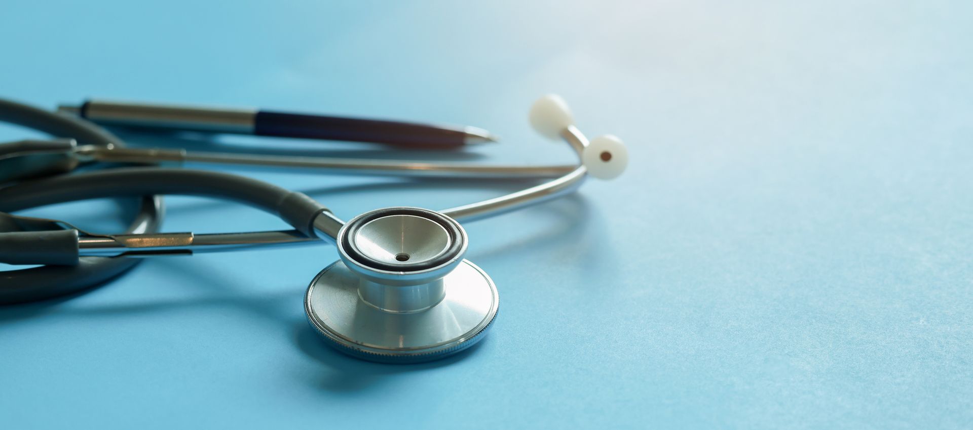 A stethoscope and pen on a light blue surface. A stethoscope and pen on a light blue surface.