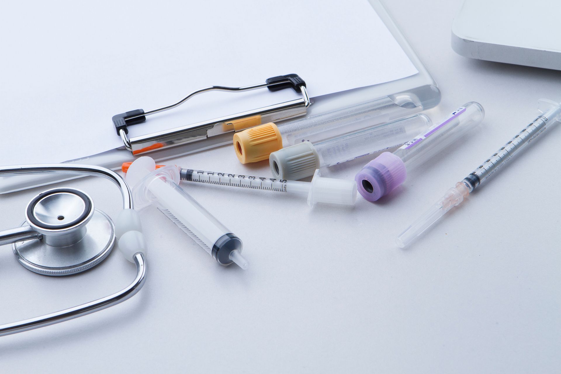 Medical equipment: stethoscope, clipboard, syringes, and vials on a white surface. Medical equipment: stethoscope, clipboard, syringes, and vials on a white surface.