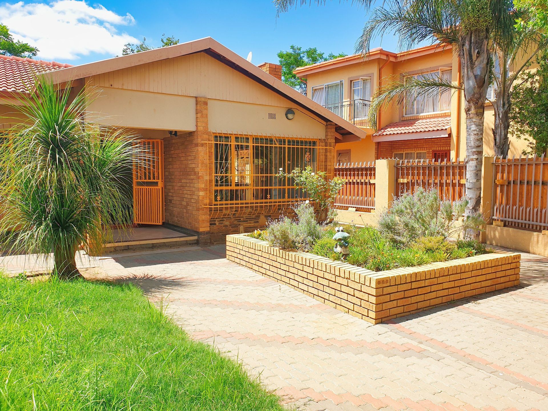 Suburban house with brick walkway, front garden, and palm trees under a bright sky