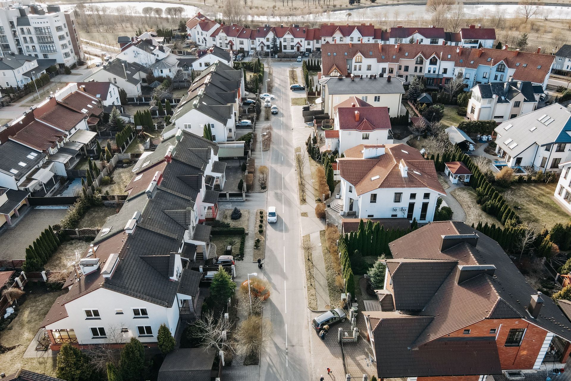 Aerial view of a suburban neighborhood with rows of houses, streets, and a central road.