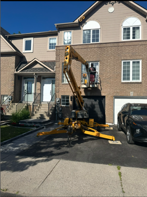 Construction lift outside townhouse, with worker on platform reaching the upper windows.