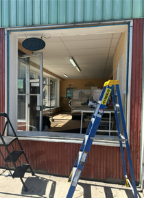 Open storefront with a blue ladder in front and a folding chair on the sidewalk
