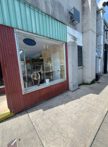 Small storefront with a large display window, red siding, and a bright sidewalk outside.