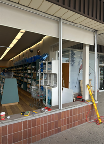 Convenience store window damaged, with broken glass and shelves visible inside