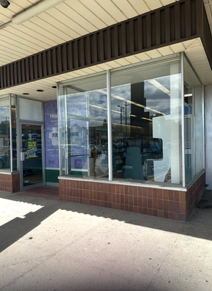 Storefront with large glass windows and brown trim on a sunny sidewalk
