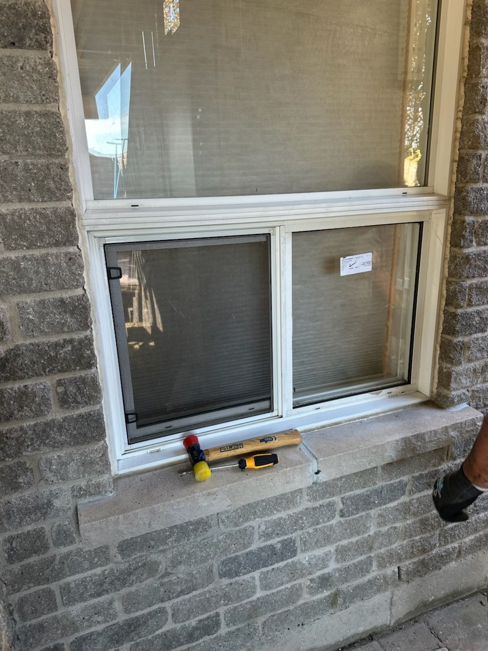 White-framed window in brick wall with tape measure and small tools on the sill