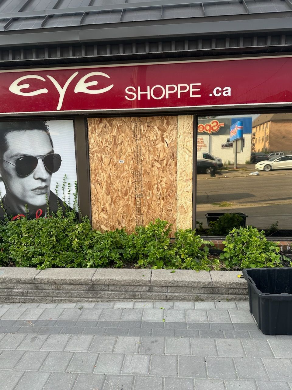 Storefront with broken boarded-up windows and a sign reading “EYE SHOPPE.ca”
