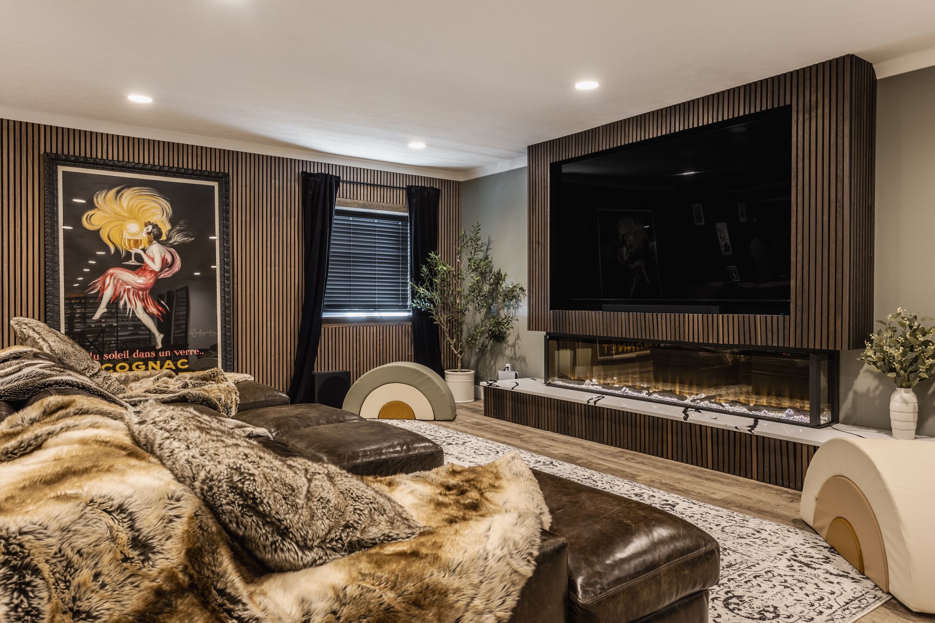 Modern open-plan basement with navy sofa, large TV, fireplace, and warm wood accents