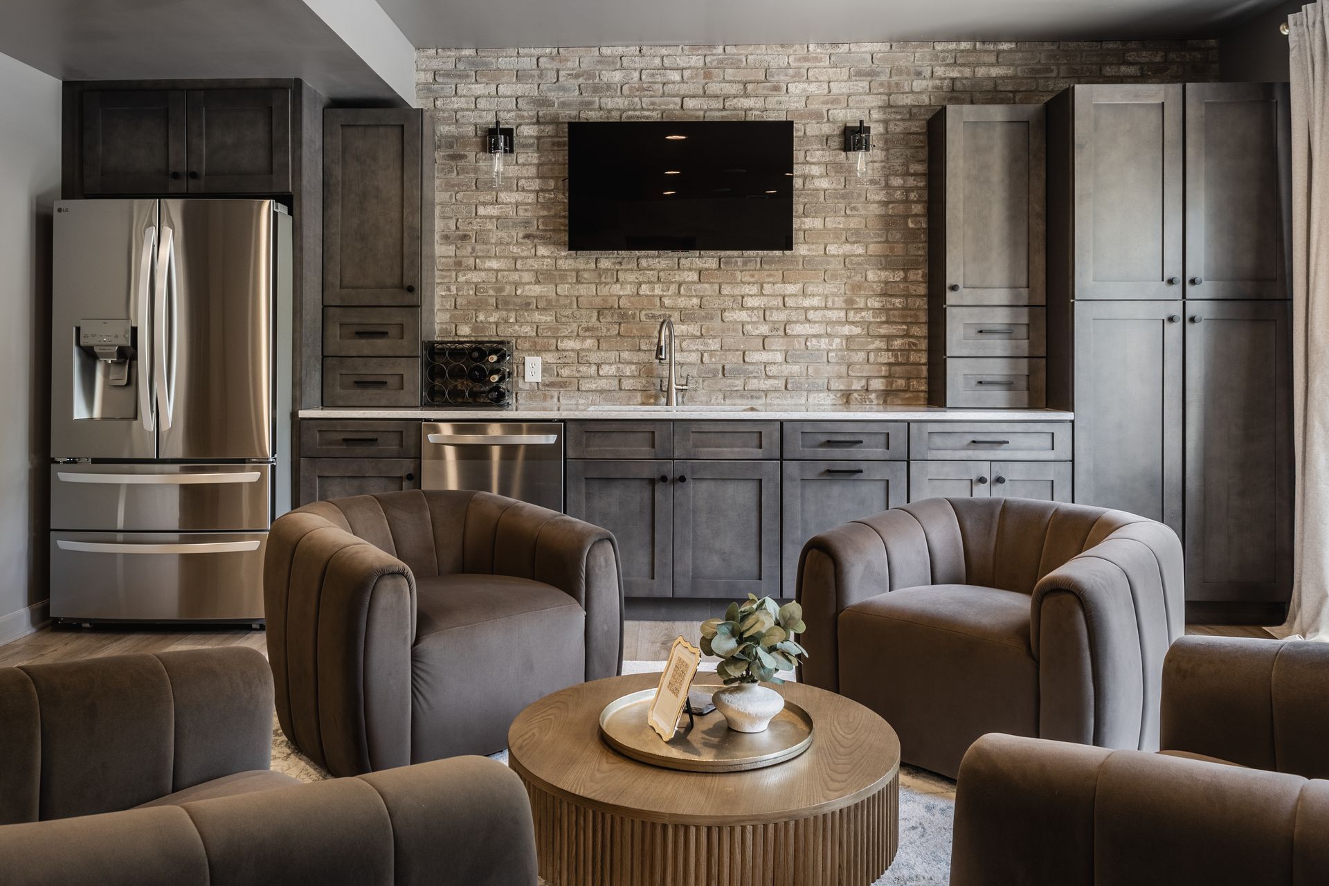 Modern open-plan basement with wood floors, recessed lights, bar stools, and a large dark dining table