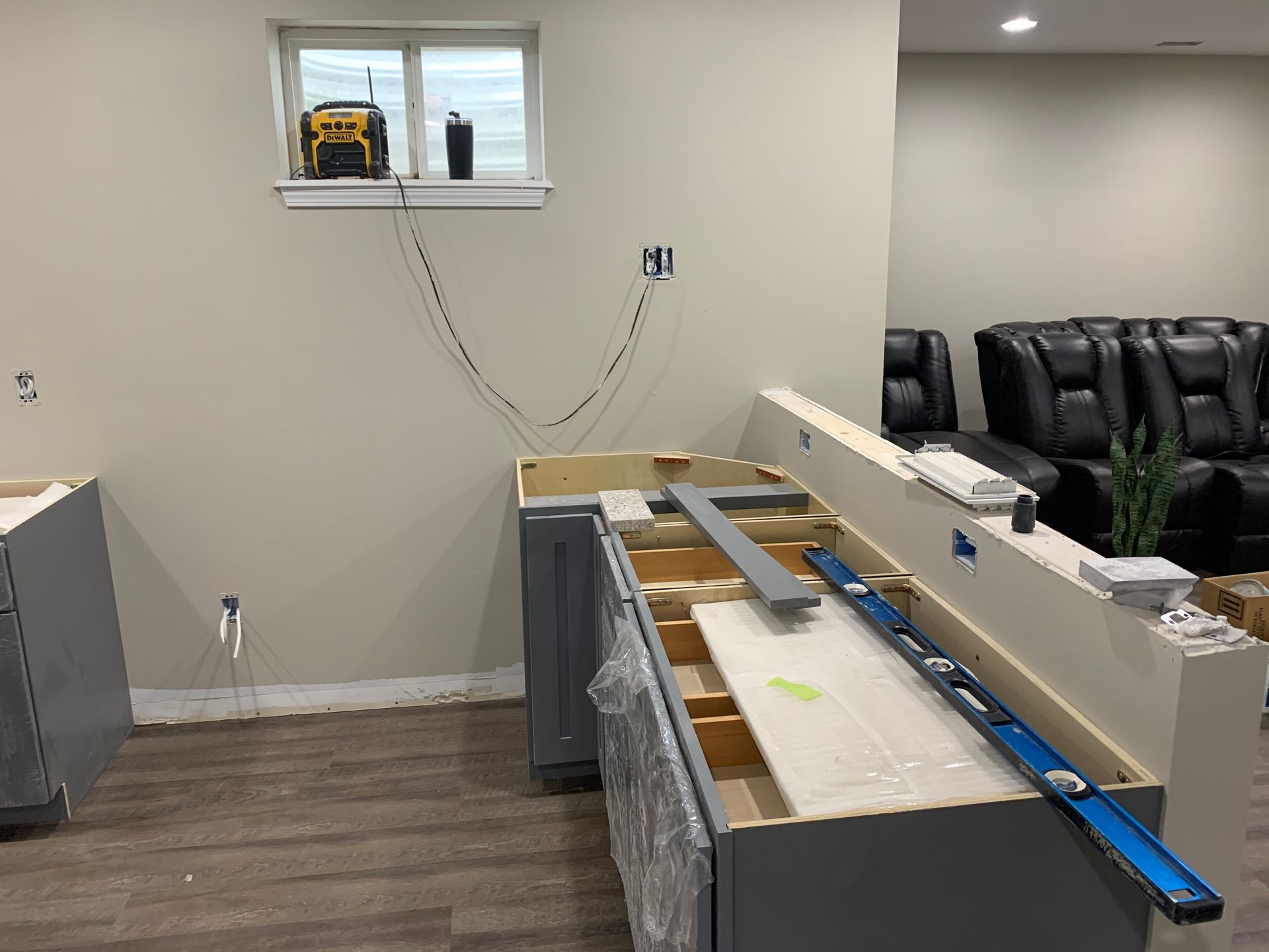 Renovated basement with unfinished cabinets, countertop, and a black leather sofa in the background