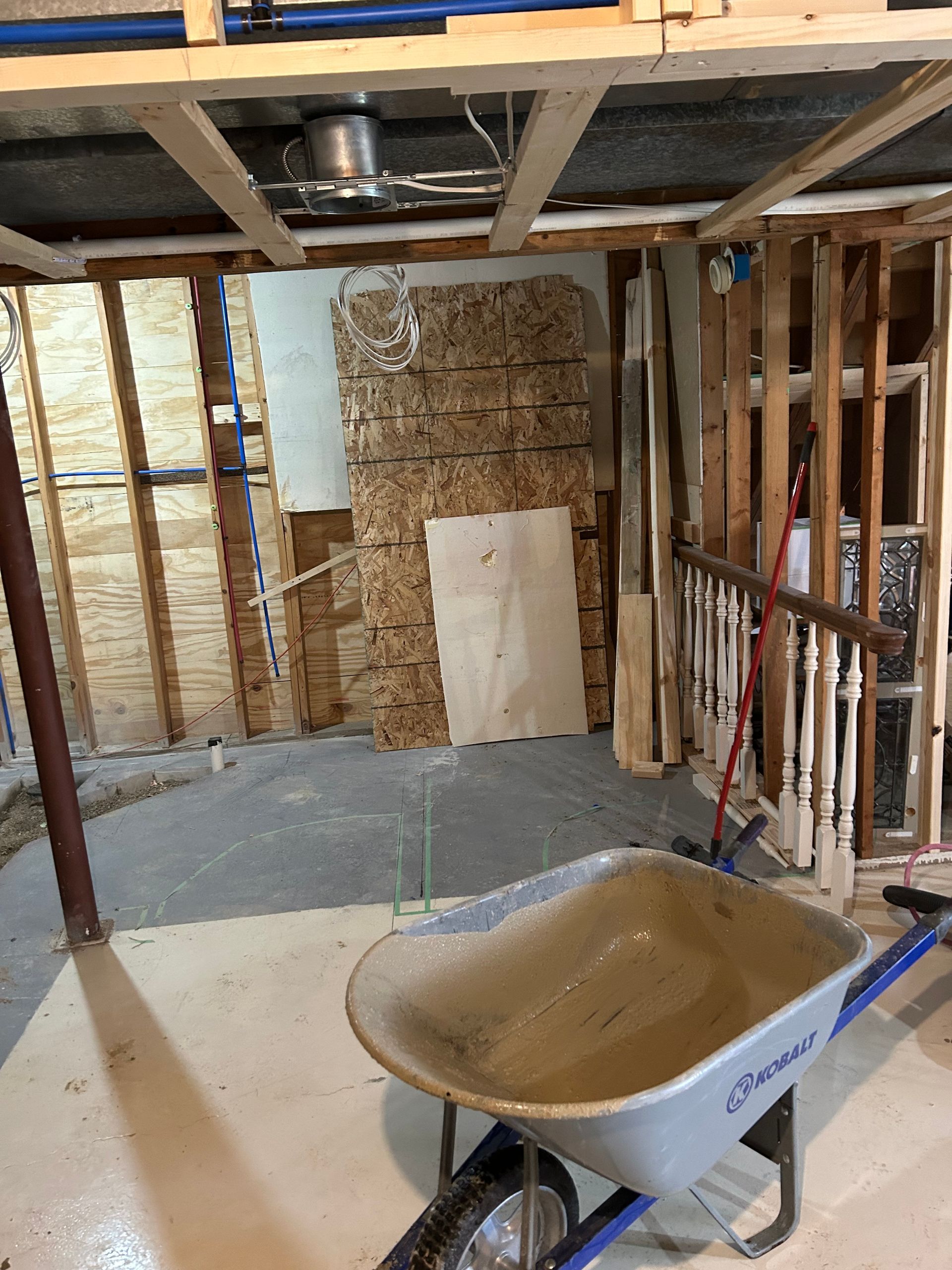 Wheelbarrow in an unfinished basement with exposed studs, insulation, and a concrete floor.