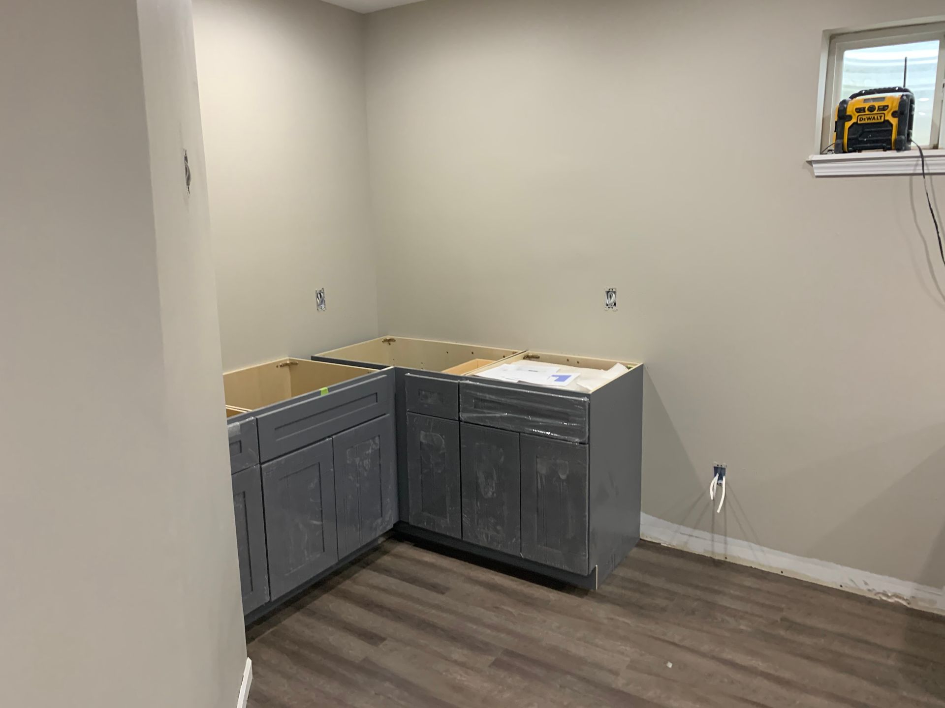 Unfinished basement with gray cabinets, wood floor, and a yellow tool on the window ledge.