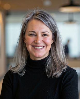 Smiling woman with gray hair in a black sweater against a blurred indoor background