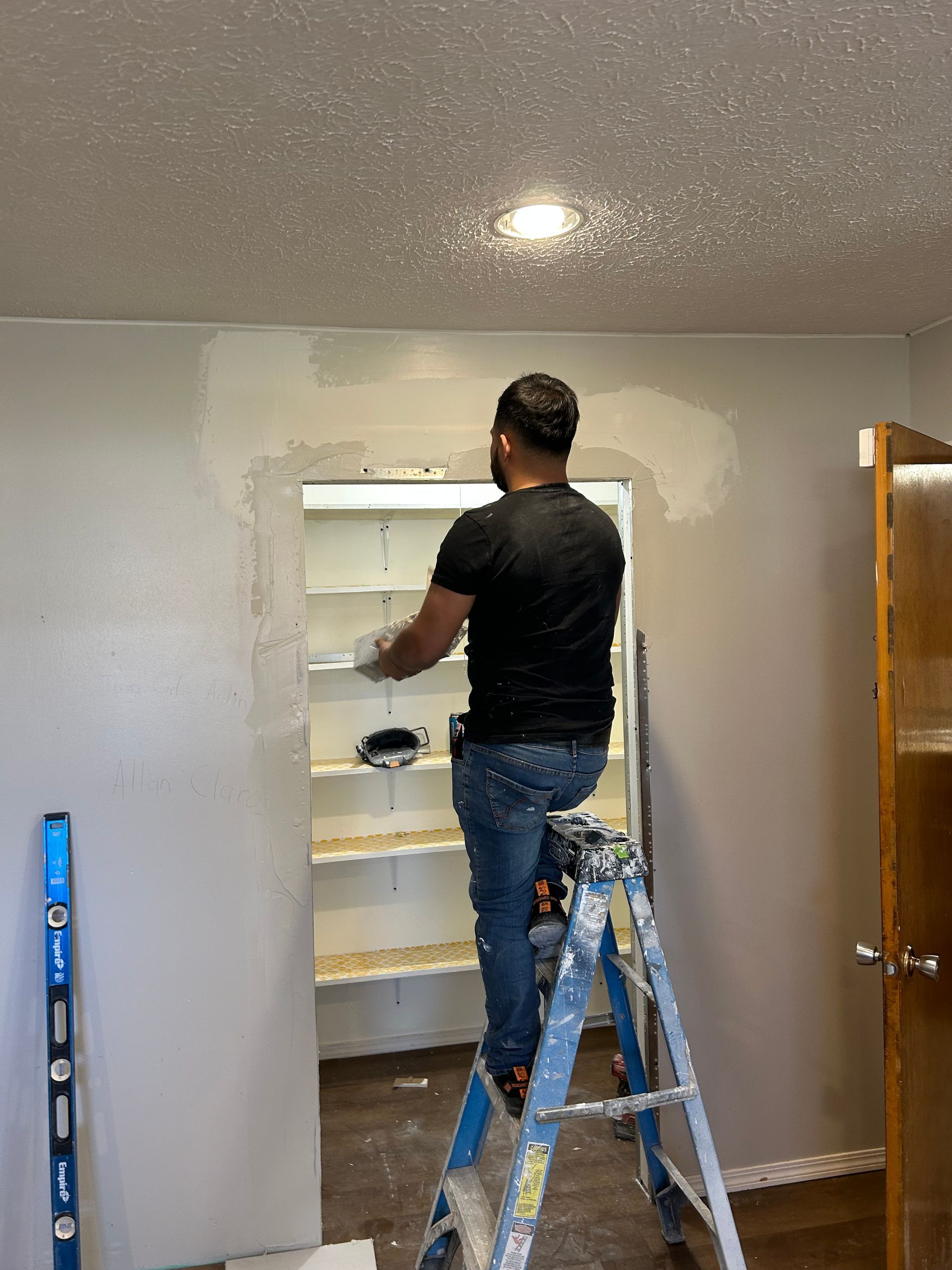 Person painting a basement closet opening in a room while standing on a step ladder