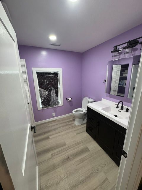 Purple bathroom in a basement with white vanity, black cabinets, toilet, and a frosted window.