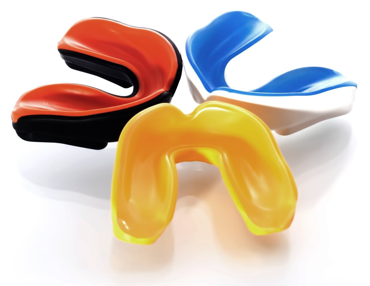 Three mouth guards of different colors are sitting on a white surface