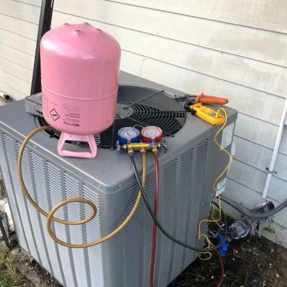 An air conditioning unit being serviced with a pink refrigerant tank, hoses, and gauges.