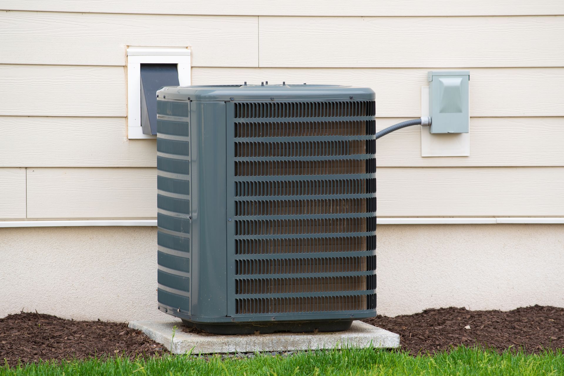 Air conditioner unit on a concrete pad outside a building with tan siding.