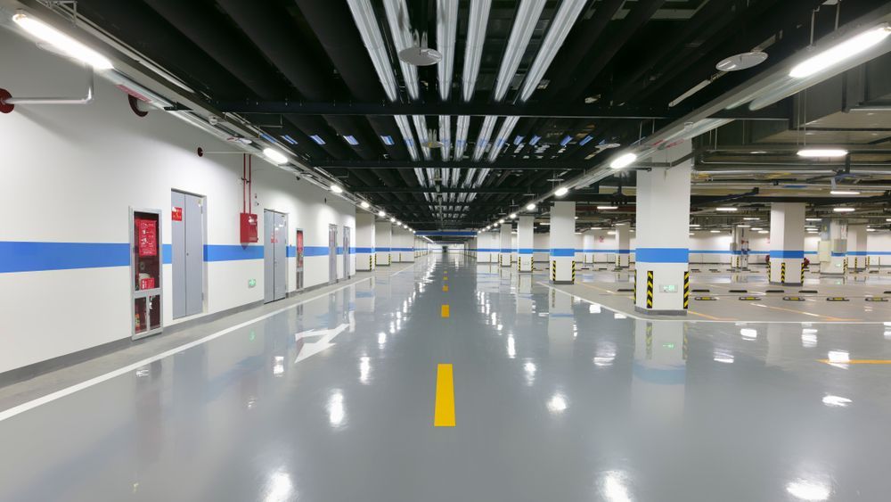 Empty underground parking garage with polished gray floor, white pillars, and yellow center line