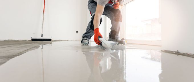 Worker spreading white flooring compound in a bright room with a trowel
