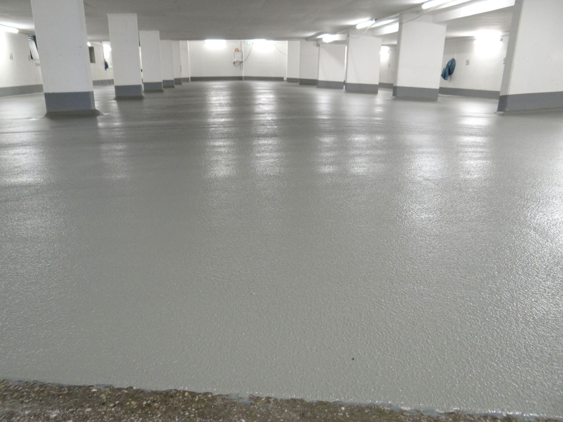Empty indoor parking garage with glossy gray floor and white support columns.